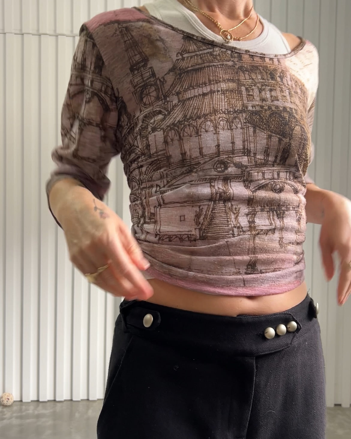 A person wears a vintage boat-neck women's top featuring a unique city-scape print over a pink and purple background