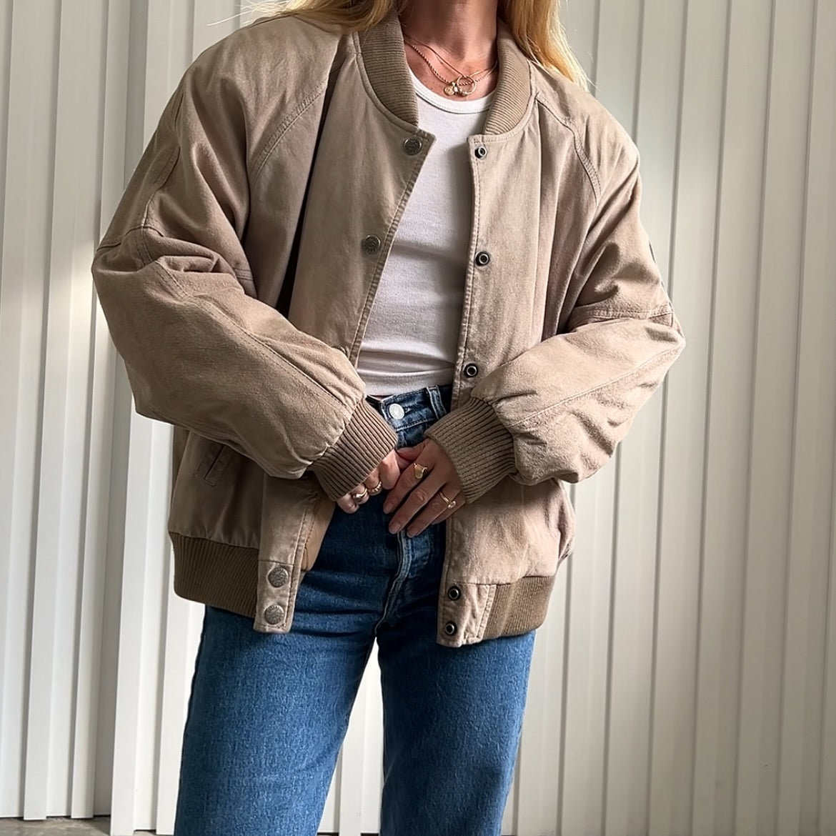 A person models a vintage brown varsity-style jacket over a white top and blue jeans